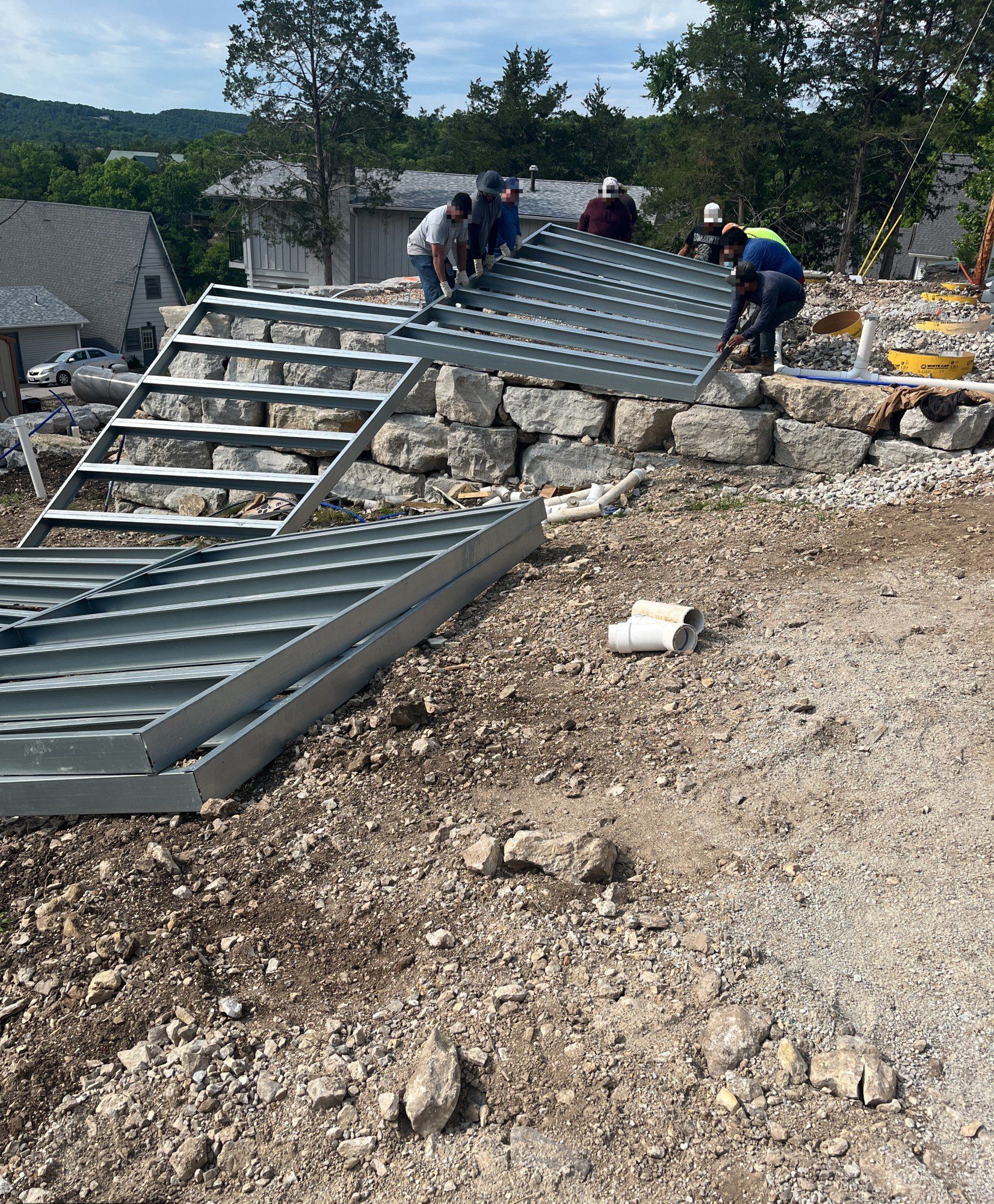 Crew of six setting galvanized steel deck frames onto a stone bank on a wooded hillside, 15 May 2026
