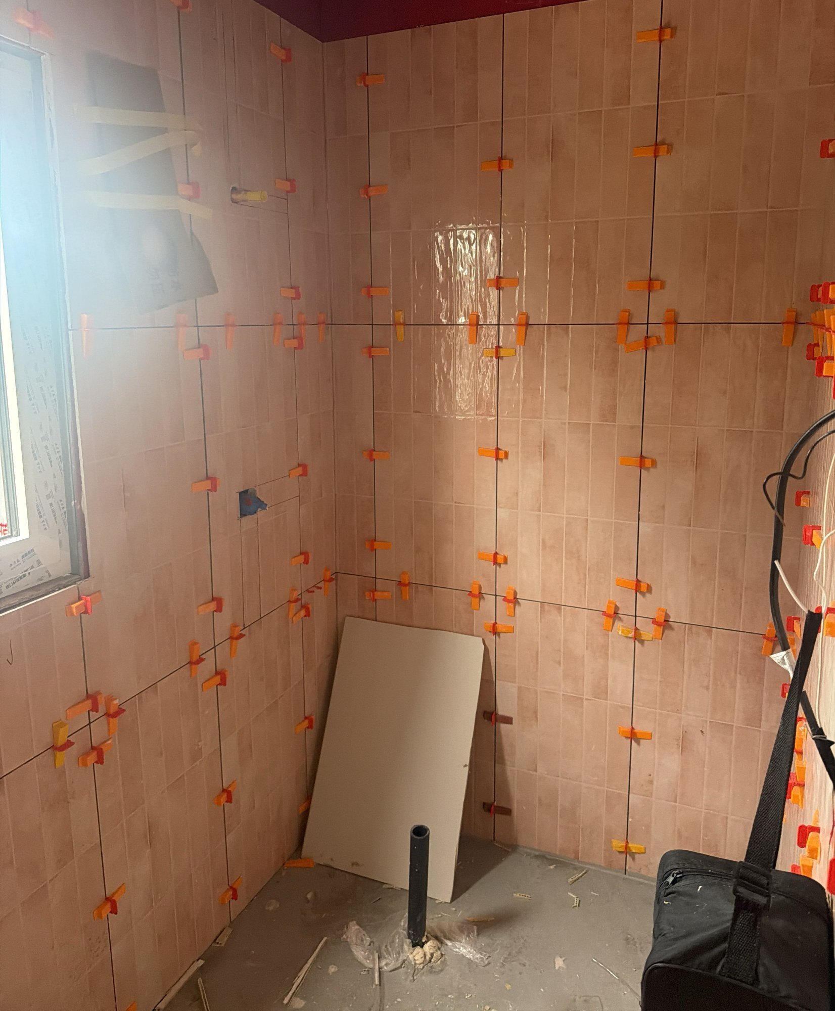 Bathroom walls tiled over a red waterproofing membrane with orange levelling clips holding each tile flush, 28 July 2026