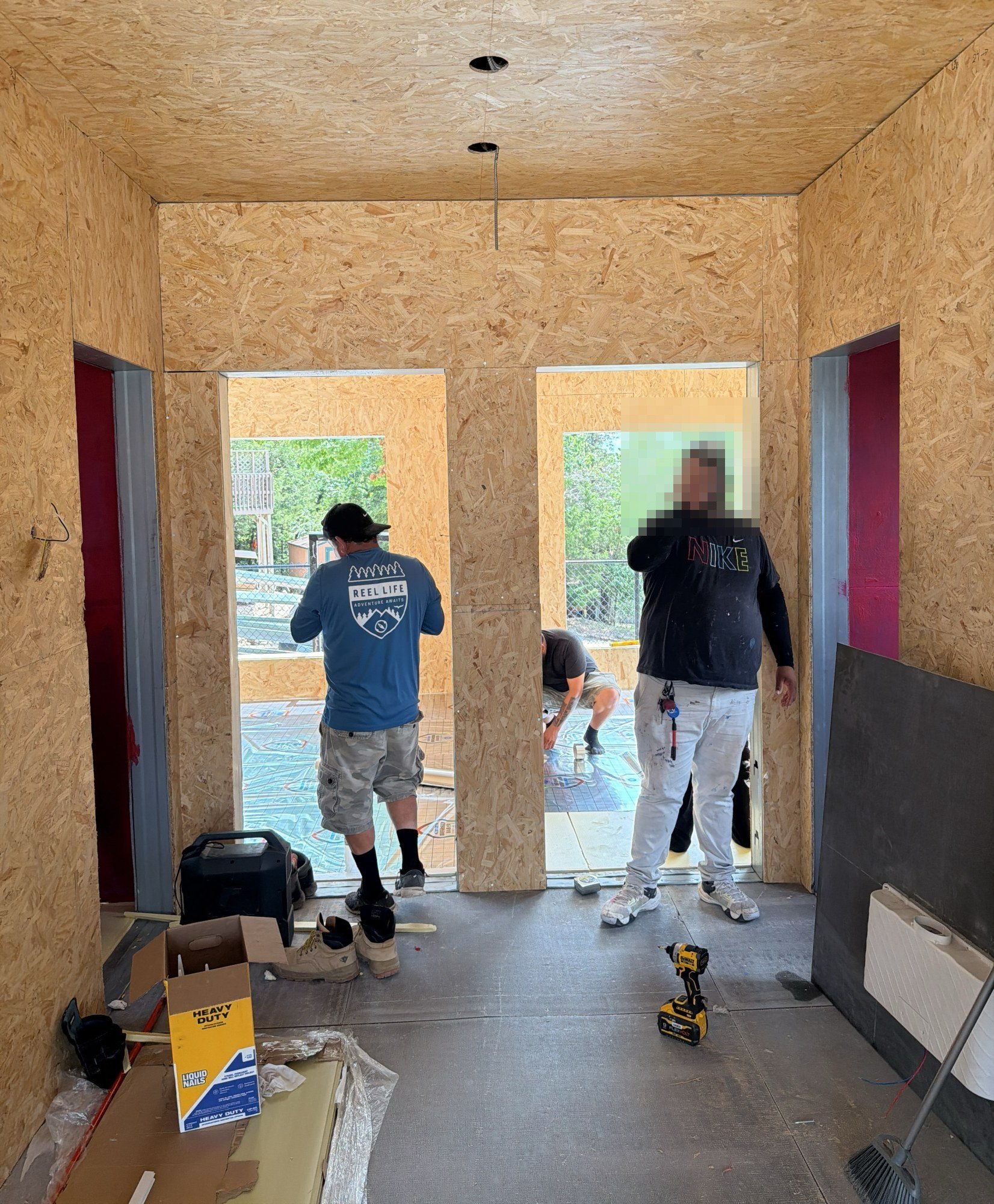 Three crew members working at two door openings in a sheathed interior wall, with tools and materials on the floor, 24 July 2026