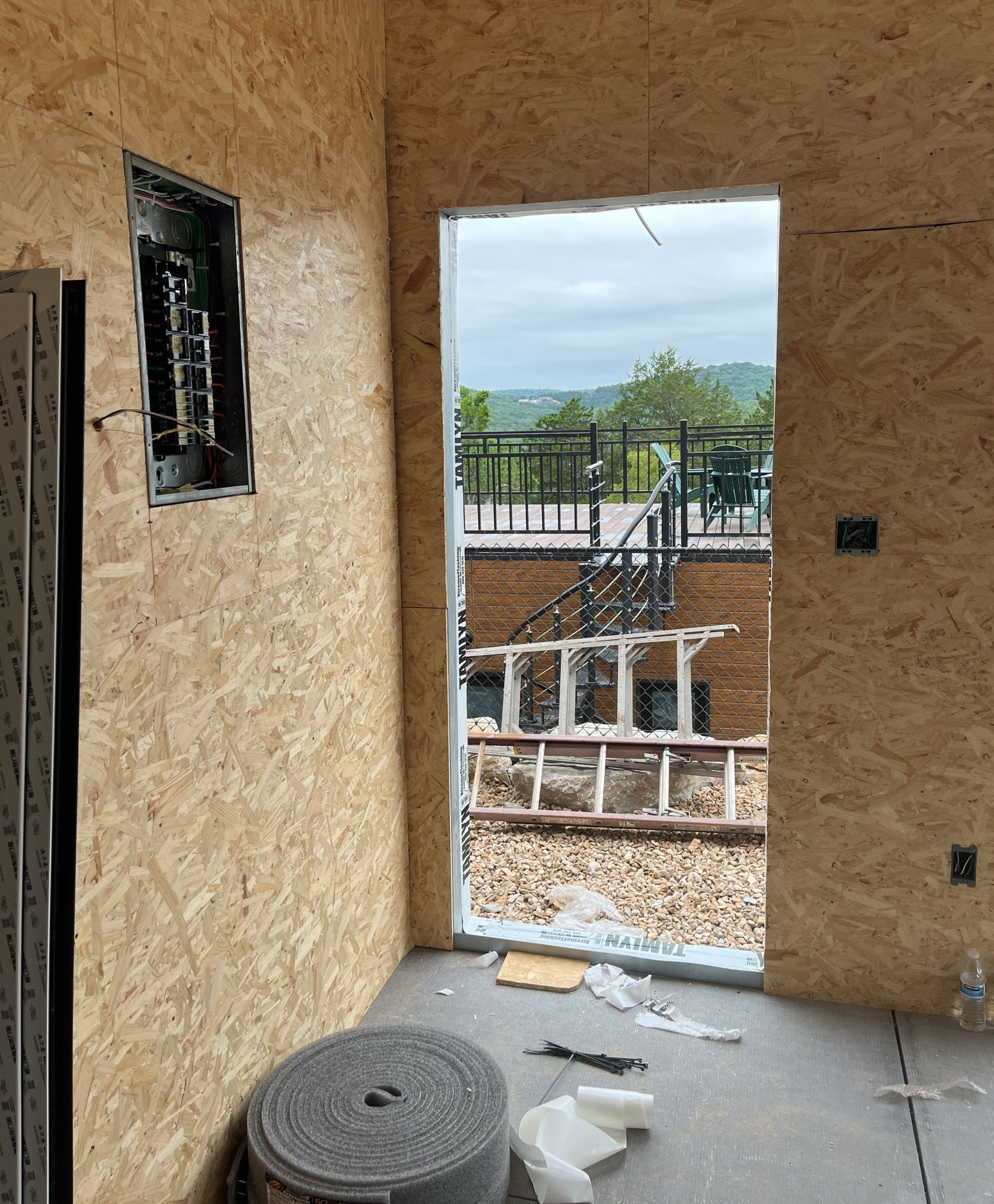 Interior room lined with oriented strand board sheathing, an electrical panel recessed in the wall and a door opening onto an outdoor deck, 24 July 2026