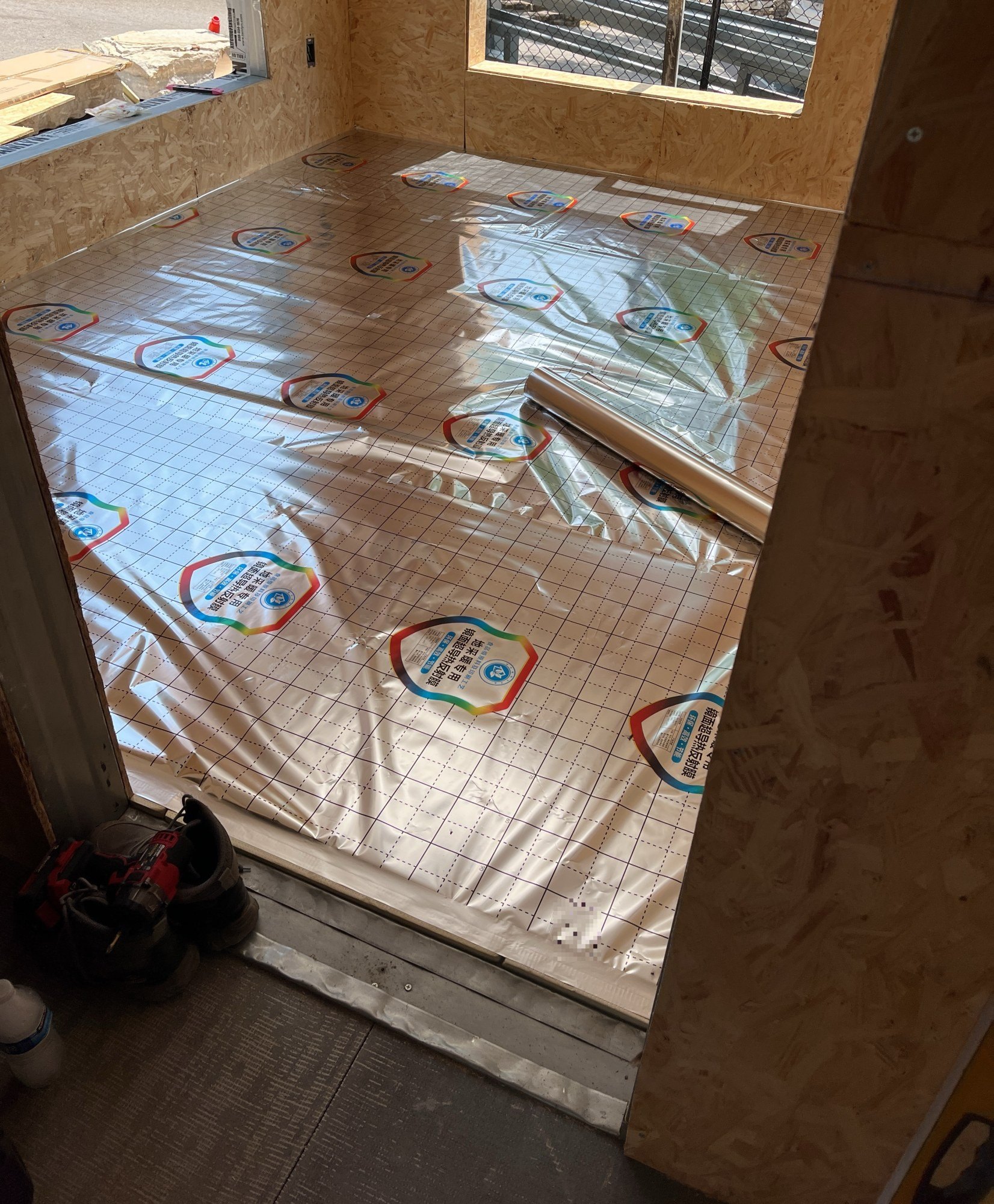 Clear protective sheeting laid across finished floor panels in a sheathed room, with a door threshold at the near edge, 24 July 2026