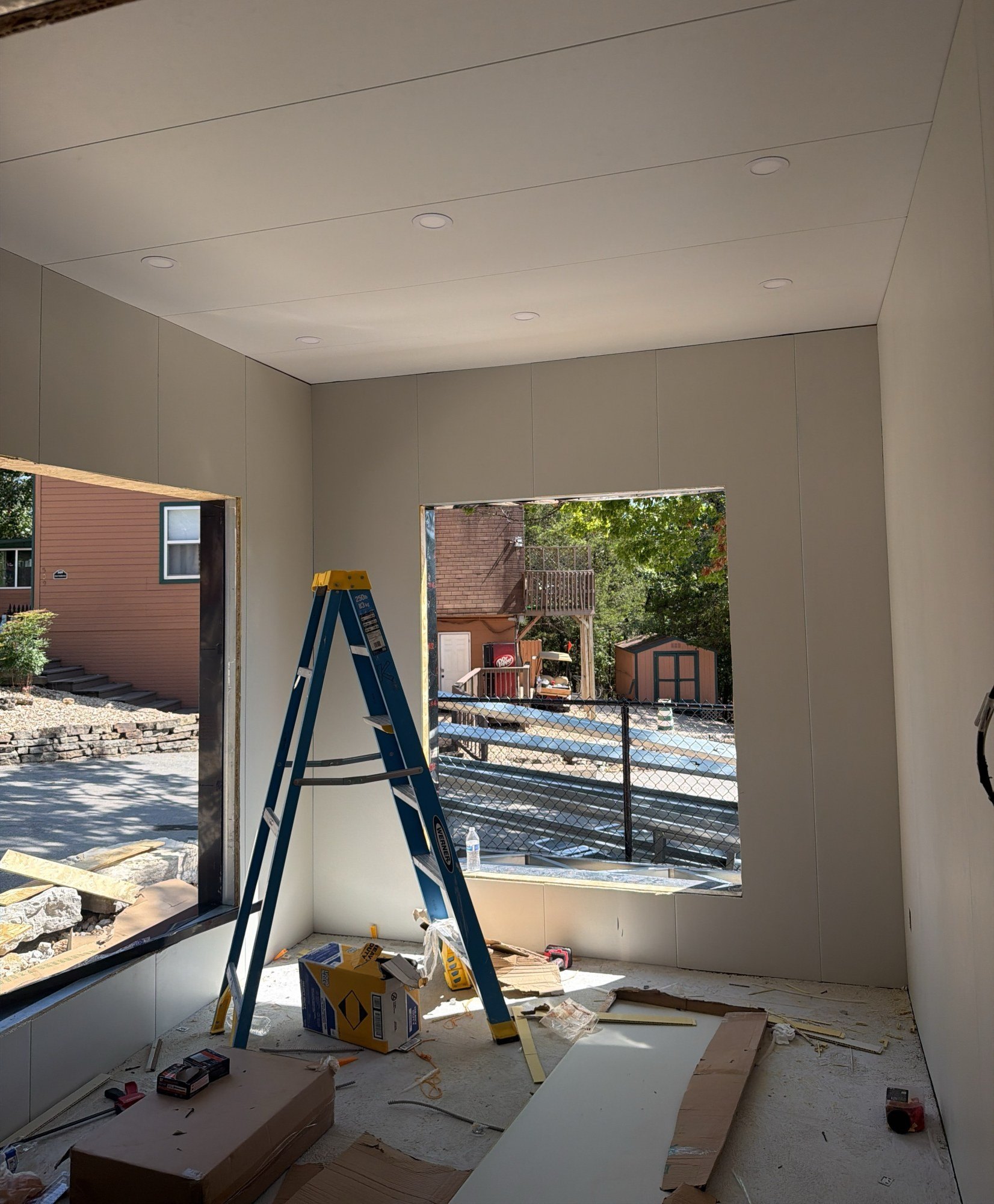 Room lined with white wall panels with windows installed, a step ladder and offcuts on the floor, 27 July 2026