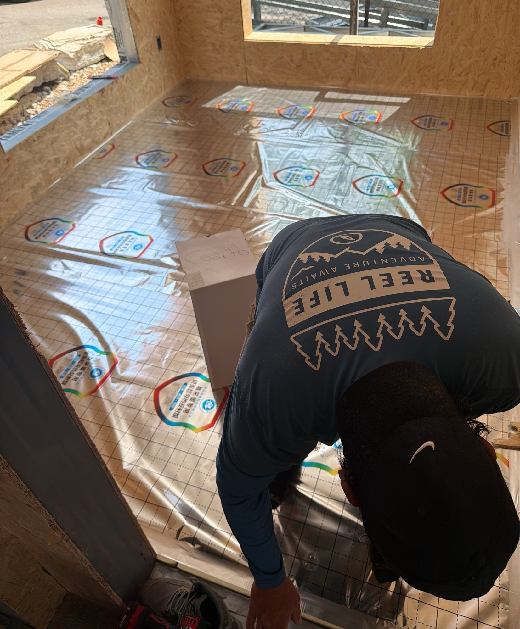 Worker bending to smooth protective sheeting across a floor in a sheathed interior room, 24 July 2026