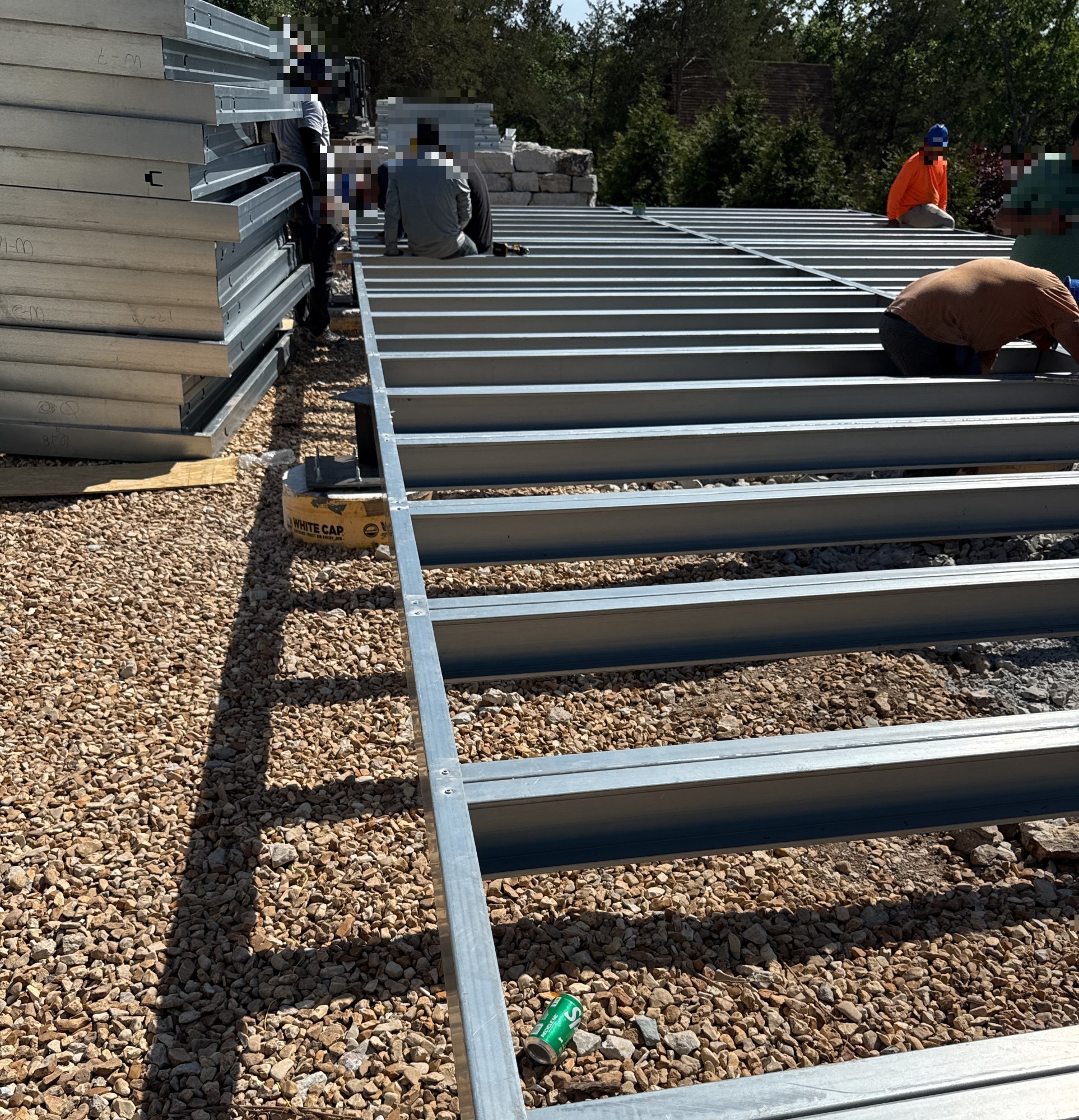 Crew setting steel floor joists across pier foundations with wall panels stacked at left, 4 May 2026